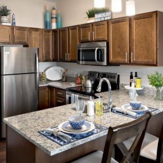 A modern kitchen with stainless steel appliances and a granite countertop, featuring a small dining setup.