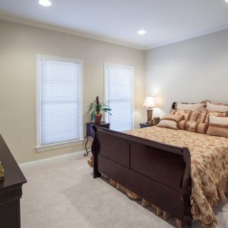 A cozy bedroom with traditional furniture, featuring a large bed, bedside lamp, and two windows letting in natural light.