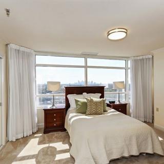 A bright and spacious bedroom with a large window, featuring a neatly made bed and matching nightstands with lamps.