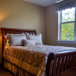 A cozy bedroom featuring a neatly made bed with decorative pillows and a window allowing natural light in.