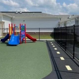 A small outdoor playground with colorful slides and a safety surface, enclosed by a fence.