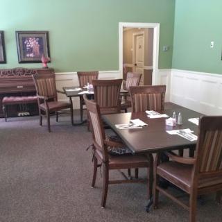 A cozy dining area featuring wooden tables and chairs, set against a calming green backdrop.