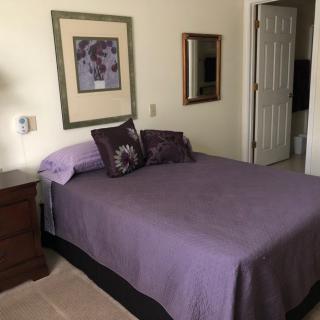 A cozy bedroom with a bed covered in a purple bedspread, accompanied by pillows and a nightstand.