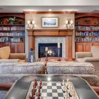 A cozy living room with a fireplace, surrounded by bookshelves and featuring a chessboard in the foreground.