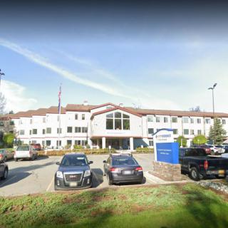 A large building with a parking lot and several cars in front, featuring a prominent entrance and signage.