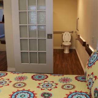 A bedroom with a colorful patterned bedspread and an adjacent accessible bathroom featuring a sliding door.
