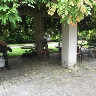 A serene outdoor gazebo with chairs and tables surrounded by lush greenery.