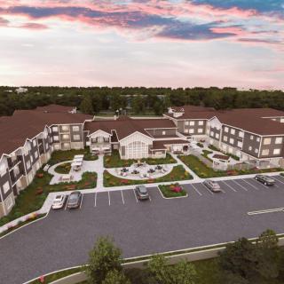 An aerial view of a residential complex with landscaped gardens and a parking lot at sunset.