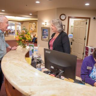 People interacting at a reception desk in a lobby.