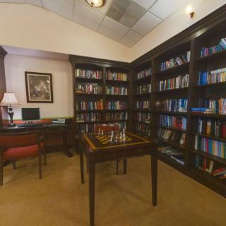 A cozy library corner with bookshelves, a chessboard, and a desk.