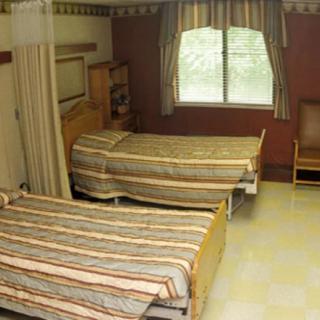 A hospital room with two beds, a window, and chairs.
