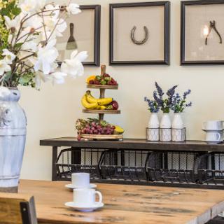 A cozy kitchen setting featuring a wooden table, decorative flowers, and a fruit stand.