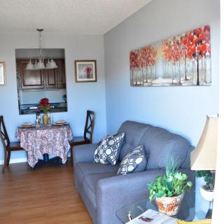 A cozy living space featuring a gray sofa, dining table, wall art, and indoor plants.