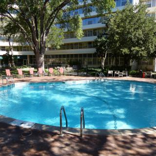 Outdoor swimming pool surrounded by trees and chairs near a building.