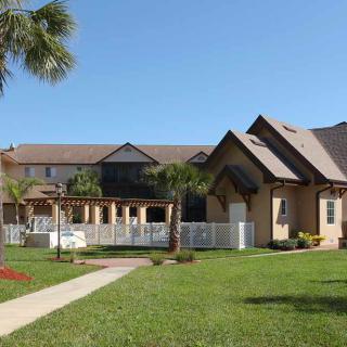 A large residential house with a well-maintained lawn and palm trees under a clear blue sky.