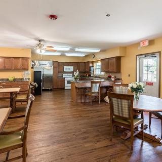 A spacious kitchen and dining area with wooden floors and yellow walls, equipped with tables, chairs, and modern appliances.