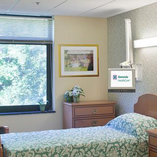 A well-lit hospital room with a single bed and a wall-mounted TV.