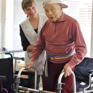 An elderly person using a walker with assistance from a caregiver during rehabilitation.