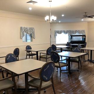 An empty dining room with several tables and chairs, a piano in the corner, and chandelier lighting.