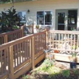 A wooden deck with railings attached to a house, surrounded by a garden.