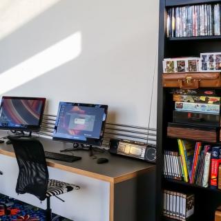 A modern workspace with dual monitors and an organized bookshelf.