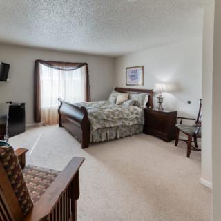 A cozy bedroom with a large bed, armchair, and a wall-mounted television.