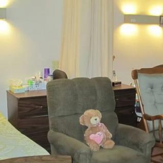 A cozy bedroom with a teddy bear on an armchair, alongside a dresser and a rocking chair.