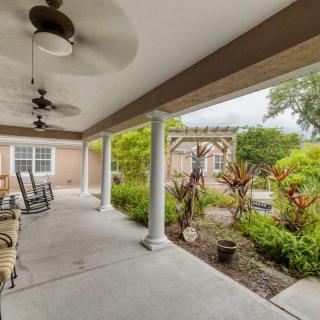A cozy patio with rocking chairs and ceiling fans overlooking a lush garden.