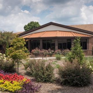 A well-maintained garden in front of a building with a red roof under a partly cloudy sky.