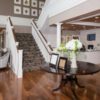 A welcoming lobby interior featuring a grand staircase, a round table with floral arrangements, and a reception area.