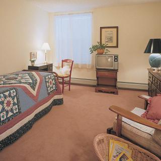 A cozy bedroom with a quilt-covered bed, a classic TV, and comfortable seating.