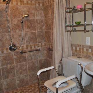 An accessible bathroom featuring a tiled shower area with a grab bar and a shower chair.