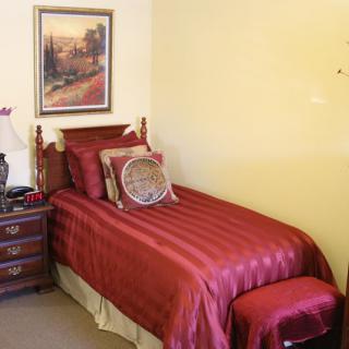 A cozy bedroom with a single bed featuring red bedding and a nightstand with a lamp.