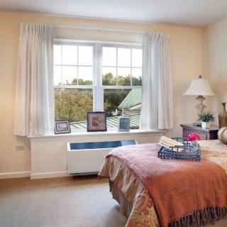 Cozy bedroom featuring a large window with curtains, a bed, and decorative elements.