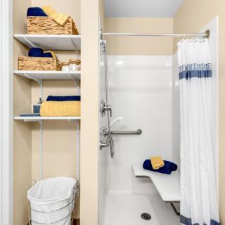An accessible bathroom with a shower, featuring storage shelves with towels and baskets.