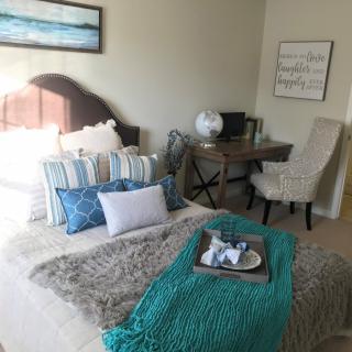 A cozy and stylish bedroom featuring a neatly made bed with decorative pillows, a throw blanket, and a small desk with a chair.