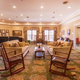 A cozy living room with comfortable sofas, rocking chairs, and a central coffee table, warmly lit with natural light streaming through the windows.