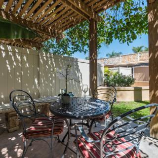 A cozy outdoor patio with a pergola providing shade over a set of table and chairs in a garden setting.