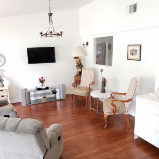 A spacious living room with elegant decor, featuring a wall-mounted television, classic chairs, a comfortable sofa, and warm wooden flooring.