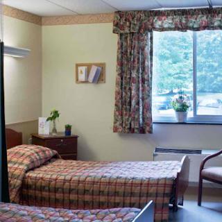 A cozy hospital room featuring two beds, a window with curtains, and decorative plants.