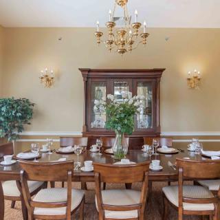 A classic dining room with an elegantly set table, chandelier, and a wooden cabinet.