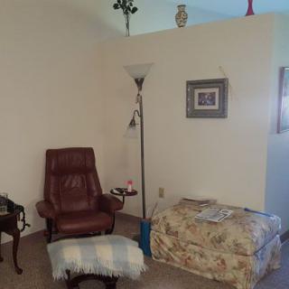 A cozy living room corner with a leather chair, a floral ottoman, and a floor lamp.