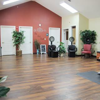 A spacious salon interior with chairs and hair dryers, featuring wooden floors and decorative plants.