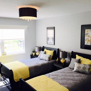 A modern bedroom featuring two twin beds with a yellow and gray color scheme, accented by stylish wall art and ample natural light.