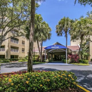 A hotel entrance surrounded by lush greenery and palm trees on a sunny day.