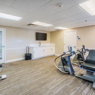 A modern gym room featuring workout equipment including an exercise bike and treadmill, with a television mounted on the wall.