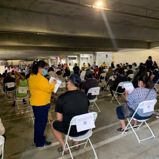 A large group of people seated in a vaccination clinic waiting area.