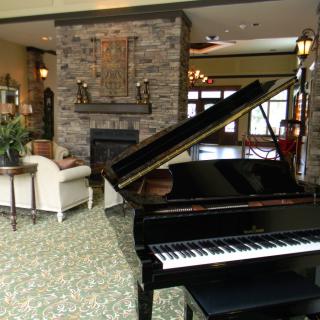 A cozy living room featuring a grand piano and stone fireplace.