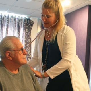 A healthcare professional using a stethoscope to examine an elderly patient.