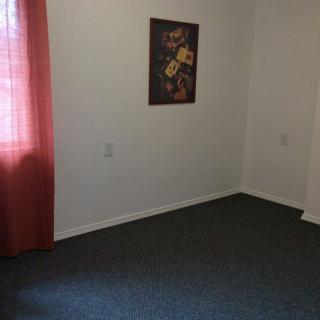 An empty room with carpeted flooring, a decorative painting on the wall, and red curtains by the window.
